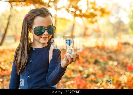 little girl with hourglass surrounded by autumn foliage Stock Photo