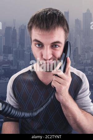 Bored young businessman talks on phone over city background Stock Photo
