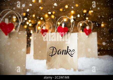 Christmas Shopping Bags On Snow With German Calligraphy Danke Means Thank You. Bright Glowing Lights In Background And Snowflakes Stock Photo