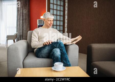 Adult man sitting on couch and reading newspaper at home. Mature male person relaxes in armchair Stock Photo