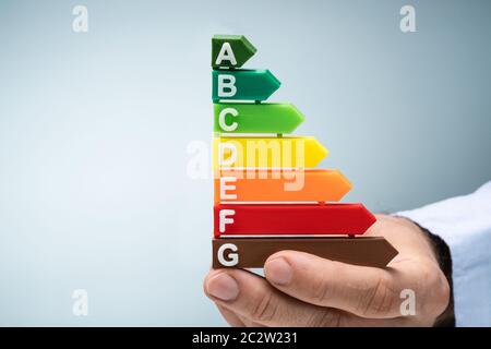 Close-up Of A Man's Hand Holding Plastic Energy Efficiency Graph Against Blue Background Stock Photo