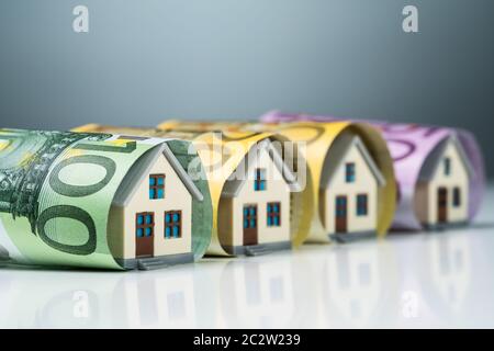 Row Of Miniature Houses Inside The Euro Banknotes On White Desk Against Gray Background Stock Photo
