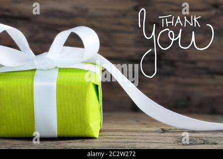 Label With English Calligraphy Thank You. One Green Gift With White Bow. Brown Wooden Background Stock Photo