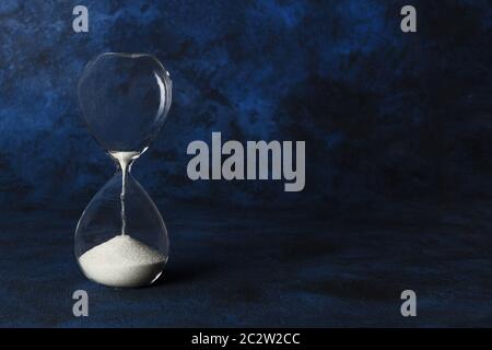 Time is running out concept. An hourglass with sand falling through, on a dark blue background with copy space Stock Photo