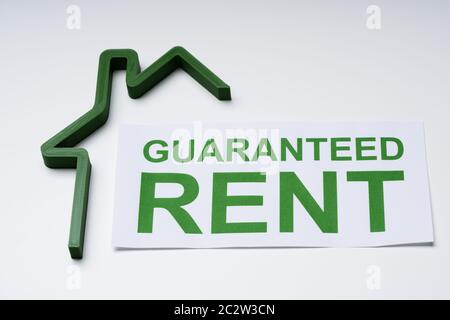High Angle View Of Green House Model And Paper With Guaranteed Rent Text Stock Photo