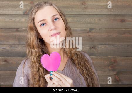 Young woman with funny pink heart in hand, wooden background. Fun photo props and accessories for shoots Stock Photo