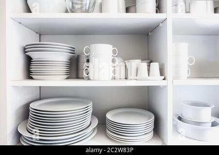 White Cupboard with white crockery in the kitchen, various clean dishes close-up Stock Photo
