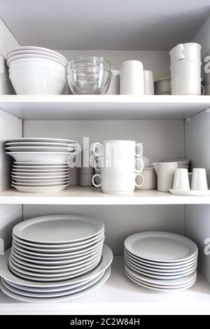 White Cupboard with white crockery in the kitchen, various clean dishes close-up Stock Photo