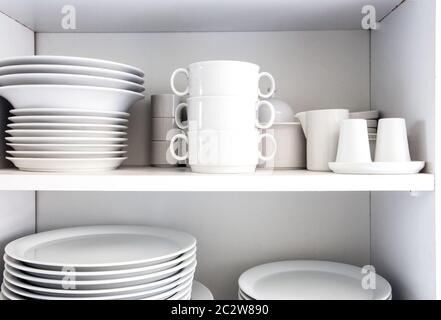 White Cupboard with white crockery in the kitchen, various clean dishes close-up Stock Photo