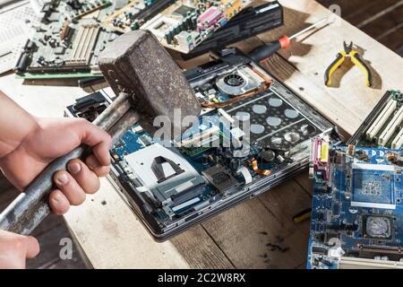 Male hands with sledgehammer brakes laptop and computer electronic components closeup view. Engineering humor Stock Photo