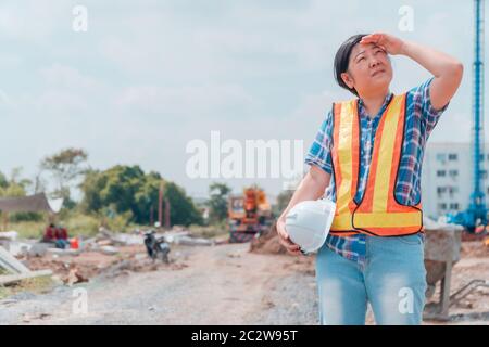 Engineering woman holding a white safety helmet standing In front of the construction site. Concepts for controlling and checking the construction acc Stock Photo