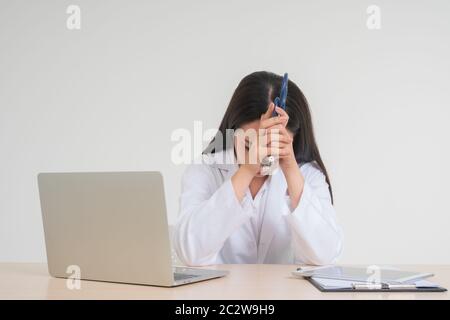 Young Asian woman doctor sitting on desk, she look unhappy and tired because of overwork, Concept of stressed exhausted and doctor liability, Dealing