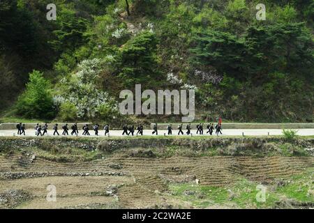 North Korea, Pyongyang - April 30, 2019: A group of North Korean soldiers with red flag marching along the road in countryside. DPRK Stock Photo