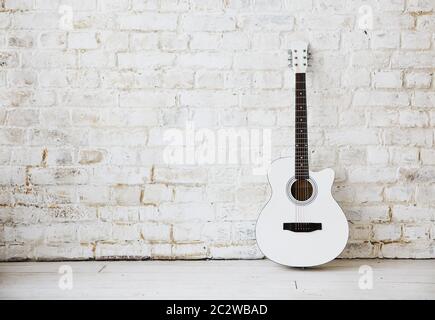 Acoustic white guitar leaning against a white wall in an empty room Stock Photo