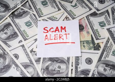 Background Of Dollar Bills With Scam Alert Text Written With Marker On Notepaper Stock Photo