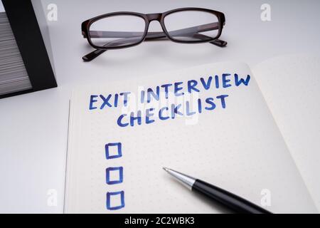 Handwritten Exit Interview Checklist Message On Notebook With Blue Marker And Spectacles Over Office Desk Stock Photo