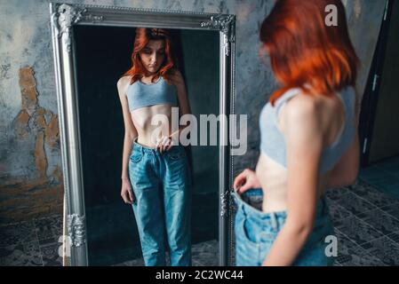 Thin woman tries on big size jeans against mirror, weight loss, anorexia. Fat or calories burning concept, medical illness Stock Photo