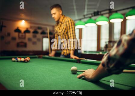 Two male billiard players with cue at the table with colorful balls. Men plays american pool in sport bar Stock Photo