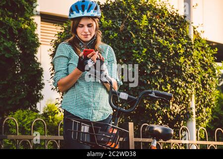 Portrait Of A Cheerful Girl Holding Mobile Phone. Happy smiling student using bike sharing app on smart phone outdoor. City life Stock Photo