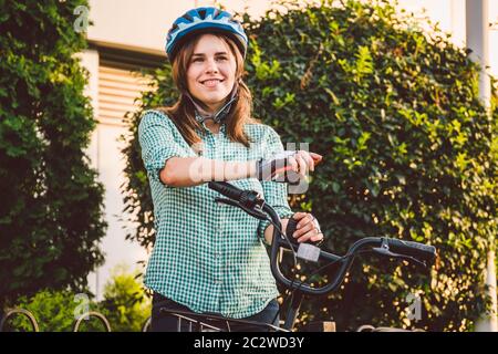 Portrait Of A Cheerful Girl Holding Mobile Phone. Happy smiling student using bike sharing app on smart phone outdoor. City life Stock Photo