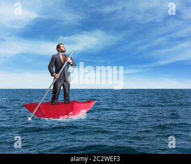 Confident businessman in the umbrella sails in calm sea Stock Photo