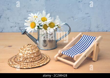 small miniature lounger , straw hat and watering can with daisies on table with blue background Stock Photo
