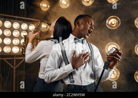 Male jazz performer and female saxophonist with saxophone, performing on the stage with spotlights. Jazz players playing on the scene Stock Photo