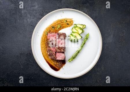 Barbecue dry aged wagyu fillet steak on hot smoked sauce with grilled green asparagus and sliced zucchini as top view on a moder Stock Photo
