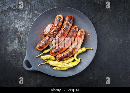Traditional barbecue German Bratwurst with hot sauce and peperoni as closeup on a modern design cast iron plate