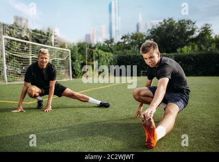 Two male soccer players doing stretching exercise on the field. Football training on outdoor stadium, team workout before game Stock Photo