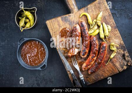 Traditional barbecue German Bratwurst with hot sauce and peperoni as top view on an old cutting board with copy space