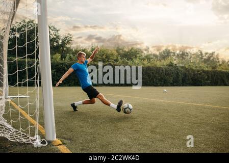 Male soccer goalkeeper hits the ball and saves the gate. Footballer on outdoor stadium, workout before game, football training Stock Photo