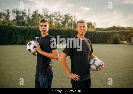 Two male soccer players holding balls in hands on the field. Footballer on outdoor stadium, workout before game, football training Stock Photo