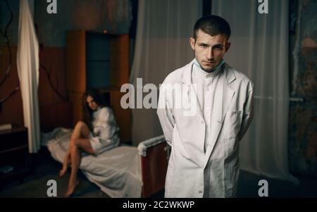 Psychiatrist and crazy female patient in strait jacket, mental hospital. Woman in straitjacket undergoing treatment in clinic for the mentally ill Stock Photo