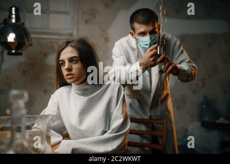 Psychiatrist with syringe preparing to give a sedative injection to crazy female patient, mental hospital. Woman undergoing treatment in clinic for th Stock Photo