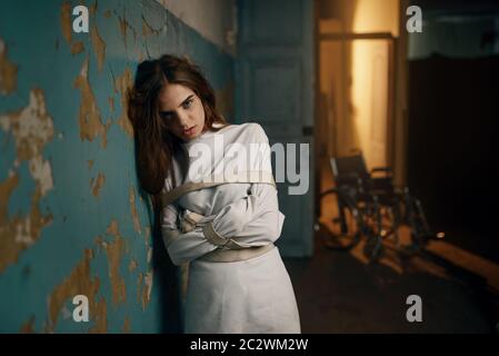 Crazy female patient in strait jacket, mental hospital. Woman in straitjacket undergoing treatment in clinic for the mentally ill Stock Photo