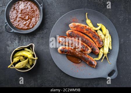 Traditional barbecue German Bratwurst with hot sauce and peperoni as top view on a modern design cast iron plate