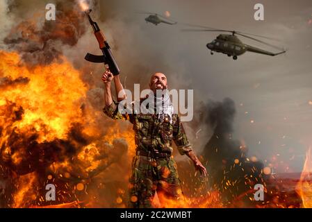 Bearded terrorist with rifle in hands stands in explosion and fire. Terrorism and terror, soldier in khaki camouflage, military helicopters in the sky Stock Photo