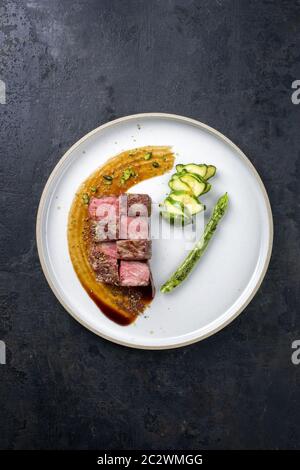Barbecue dry aged wagyu fillet steak on hot smoked sauce with grilled green asparagus and sliced zucchini as top view on a moder Stock Photo