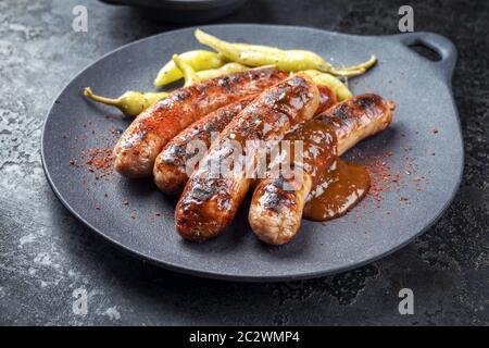 Traditional barbecue German Bratwurst with hot sauce and peperoni as closeup on a modern design cast iron plate