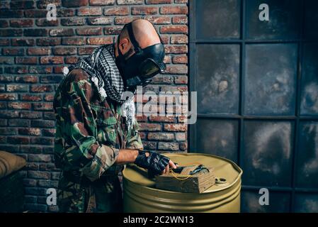 Terrorist in gas mask with kalashnikov rifle, male mujahedin with weapon. Terrorism and terror, soldier in khaki camouflage, barrels of fuel or chemic Stock Photo