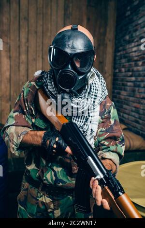 Terrorist in gas mask with kalashnikov rifle, male mujahedin with weapon. Terrorism and terror, soldier in khaki camouflage, barrels of fuel or chemic Stock Photo