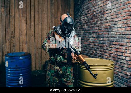 Terrorist in gas mask with kalashnikov rifle, male mujahedin with weapon. Terrorism and terror, soldier in khaki camouflage, barrels of fuel or chemic Stock Photo