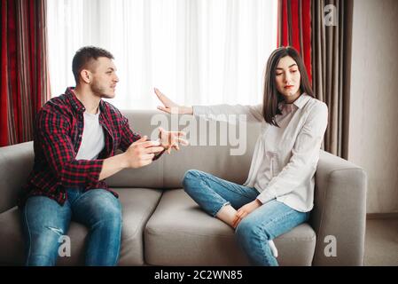 Stressed wife sits on couch, angered husband yells on her, family conflict. Unhappy man and woman in quarrel Stock Photo