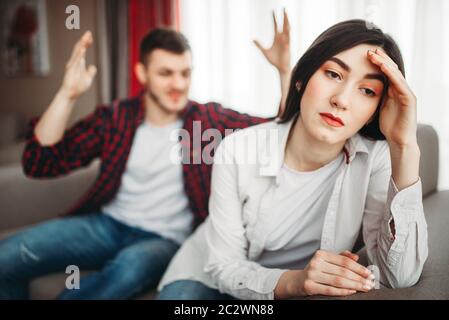 Stressed wife sits on couch, angered husband yells on her, family conflict. Unhappy man and woman in quarrel Stock Photo