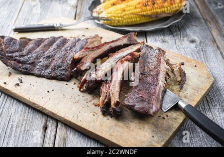 Barbecue spare ribs St Louis cut with hot rub and corn as closeup on a wooden cutting board Stock Photo