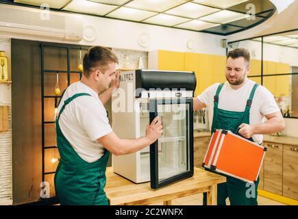 Male workers in uniform repair refrigerator at home. Repairing of fridge occupation, professional service Stock Photo