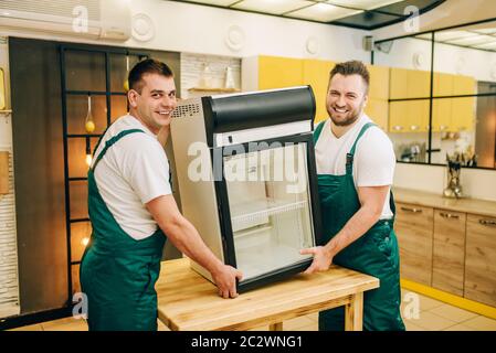 Workers in uniform installs refrigerator at home. Repairing of fridge occupation, professional service Stock Photo