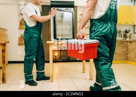 Male workers in uniform repair refrigerator at home. Repairing of fridge occupation, professional service Stock Photo