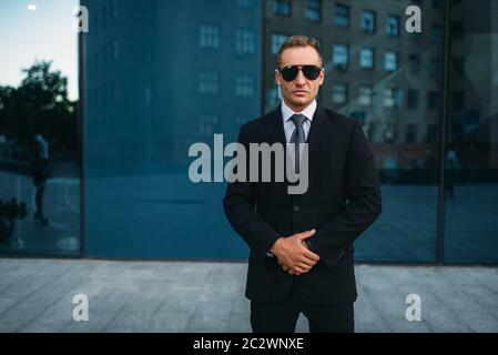 Male bodyguard in suit, security earpiece and sunglasses outdoors. Professional guarding is a risky profession Stock Photo